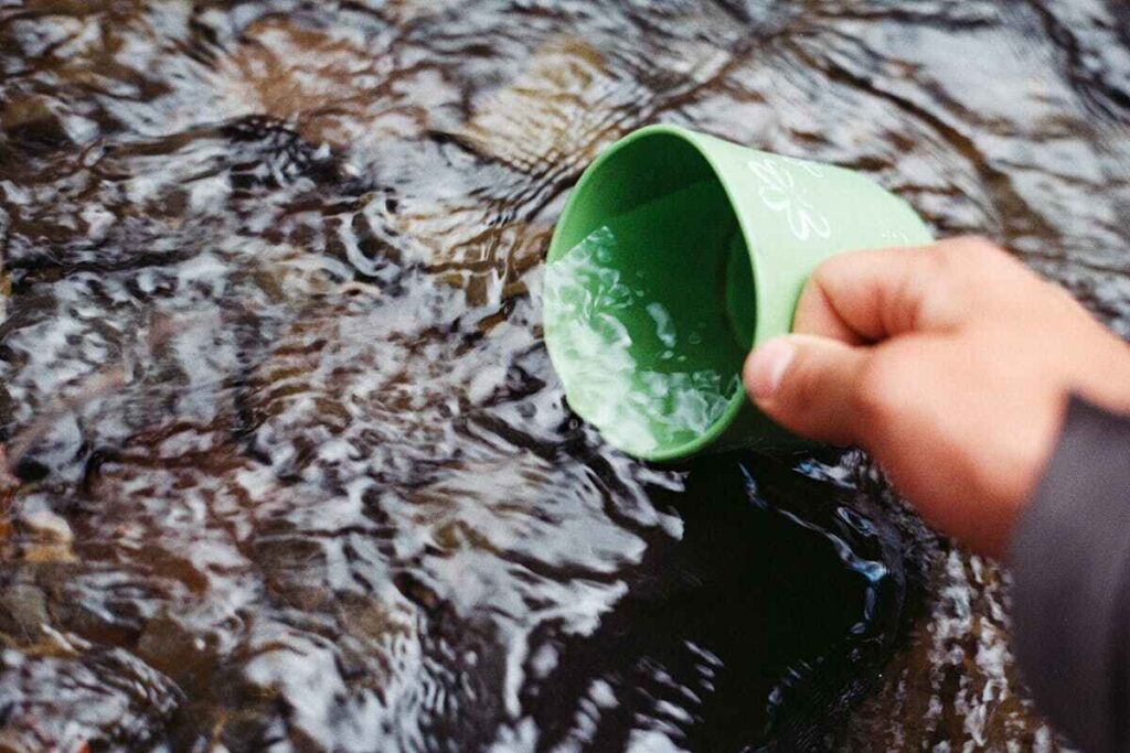 Moses West: un uomo riempie d'acqua una tazza in un fiume